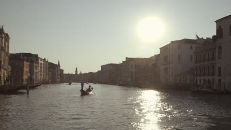 Gondola-sailing-in-Canal-Grande-lit-by-warm-sunrise-with-water-reflections,-Venice,-Italy