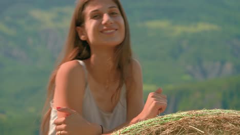 Close-up-of-a-beautiful-brunette-womansmiling-and-laughing-while-leaning-against-a-large-bale-of-hay-on-a-farm-in-France
