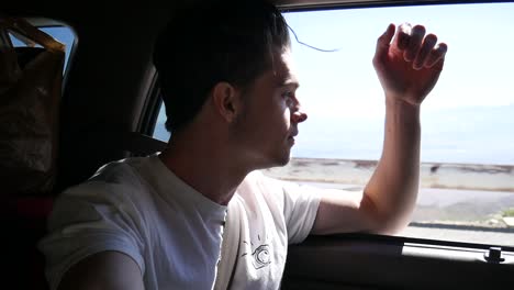 Young-happy-man-in-car-ride-looking-out-window-with-landscape-in-background