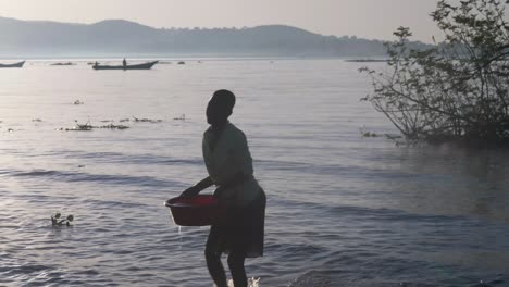 Silhouette-Einer-Afrikanerin,-Die-In-Der-Frühen-Morgensonne-Am-Ufer-Des-Lake-Victoria-Wasser-In-Einem-Eimer-Sammelt