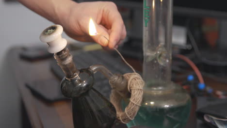 Hemp-wick-around-the-base-of-a-bong-is-lit-and-held-to-a-bowl-of-cannabis