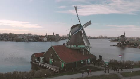 Panning-down-on-a-picturesque-view-of-a-windmill-in-the-foreground-on-a-riverbed-with-other-mills-in-the-background-and-people-walking-past