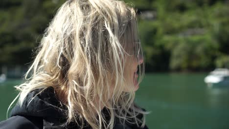 SLOWMO---Young-beautiful-caucasian-blond-girl-with-sunglasses-on-boat-in-Marlborough-Sounds,-New-Zealand