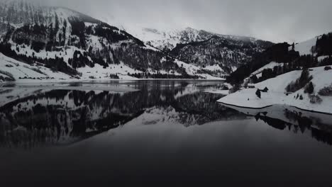 Cámara-Volando-Hacia-Atrás-E-Inclinándose-Hacia-Arriba-Para-Mostrar-El-Hermoso-Panorama-Del-Lago-De-Montaña-Invernal-En-Suiza