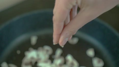 White-female-adding-salt-to-mushrooms-in-pan