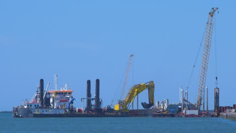 Hopper-dredger-ship-working-at-Port-of-Liepaja,-crane-with-bucket-lifts-up-soil-from-the-bay,-medium-shot-from-a-distance