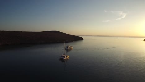 Luftaufnahme-Eines-Katamaran-Segelboots-Und-Einer-Yacht-In-Einer-Ruhigen-Bucht-Bei-Sonnenuntergang,-Meer-Von-Cortez,-Baja-California-Sur