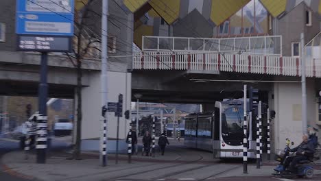 Nahaufnahme-Einer-Straßenbahn,-Die-Unter-Der-Berühmten-Architektur-Der-überhängenden-Würfelhäuser-Im-Stadtzentrum-Von-Rotterdam,-Niederlande,-Vorbeifährt