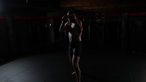 Slow-motion-of-a-mma-fighter,-covered-in-sweat,-in-a-ring,-standing-still-in-the-guard-position,-the-camera-goes-around,-in-a-dark-room,-with-a-single-light
