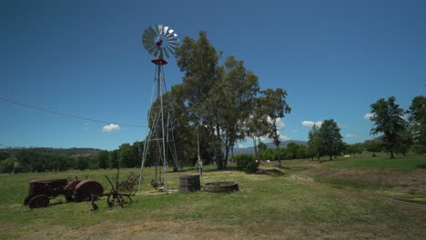Slow-motion-pan-to-the-right-of-a-windmill-on-rural-ranch-with-old-antique-tractor-in-the-foreground-in-northern-California-