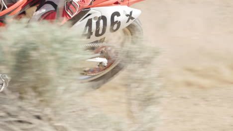 SLOW-MOTION:-A-dirt-biker-rides-his-red-motorcycle-through-the-desert-and-whips-around-a-berm