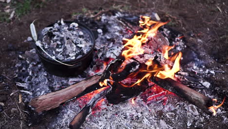 Slow-motion-shot-looking-down-at-rustic-campfire-with-camp-oven-covered-in-coals-to-the-side