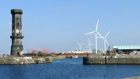 Windkraftanlagen-Drehen-Sich-In-Einem-Hafen,-Während-Eine-Große,-Kalte-Uhrturmkamera-Herauszoomt