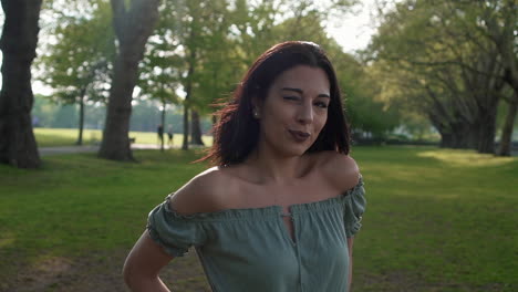 Slow-Motion-Portrait-of-a-gorgeous-hispanic-latino-young-woman-looking-at-the-camera,-blinking-and-flirting,-with-a-beautiful-British-park-in-the-background