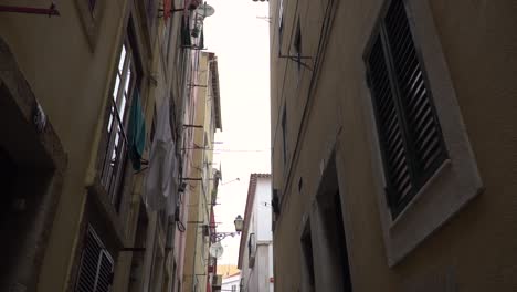POV-Cámara-Lenta-Caminando-Por-Callejones-Estrechos-En-La-Zona-De-Alfama-En-Lisboa,-Portugal-Apuntando-Hacia-Arriba