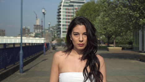 Attractive-and-playful-hispanic-latina-woman-walking-towards-the-camera,-on-the-riverbank-of-the-Thames-in-London,-UK