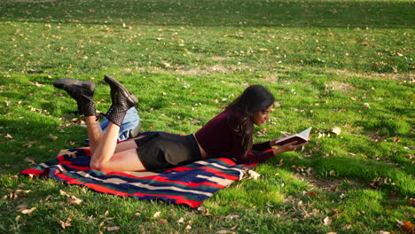 A-gorgeous-young-woman-reading-a-book-and-studying-in-a-grassy-park-field-with-autumn-leaves-blowing-in-the-wind-SLOW-MOTION