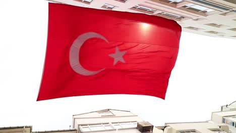 Really-big-turkish-flag-in-slow-motion-and-sunlight-leaks-between-buildings,-turkey-country