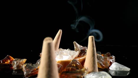 Static-shot-of-unlit-incense-cones-in-a-decorative-rock-garden,-a-lit-cone-w--smoke-flowing-in-the-back