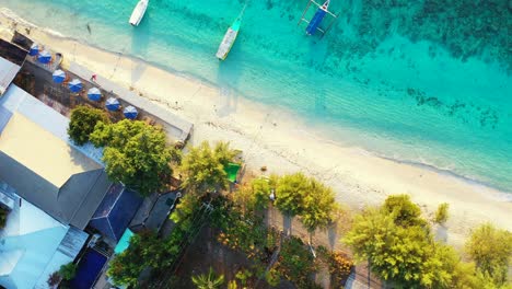 Luxury-resort-on-the-beachfront,-white-sand-beach-wavy-crystal-clear-turquoise-seawater-and-boats-moored-on-the-coast,-descending-aerial-shot