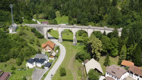 Luftaufnahme-über-Einem-Kleinen-Abgelegenen-Dorf-In-Der-Nähe-Von-Prevalje-In-Slowenien-Mit-Altem-Eisenbahnbogenviadukt-Und-Malerischer-Natur