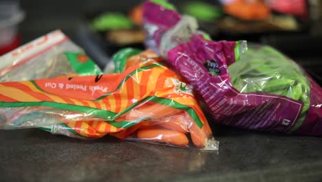 Slow-Motion-shot-panning-over-two-plastic-bags-filled-with-organic-baby-carrots-and-organic-edamame's
