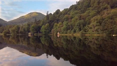 Mirror-reflection-of-hills,-woods-and-boathouses-on-Ullswater-lake