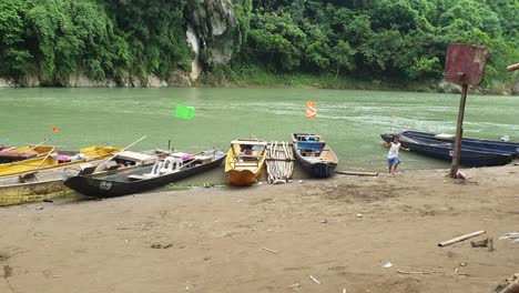 local-village-children-running,-dancing-near-the-river,-boats-seen-on-background
