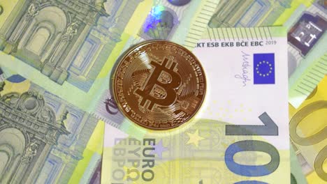 Tiro-Giratorio-De-Bitcoin-Dorado-Brillante-Sobre-Una-Capa-De-Billetes-De-Cien-Euros