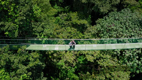 Aerial-Drone-shot-with-Top-Down-Camera-of-Couple-Enjoying-the-View-on-Hanging-Footbridge-in-the-Middle-of-the-Rain-forest-in-Arenal,-Costa-Rica