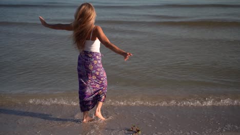 Closeup-slow-motion-of-mature-woman-in-sarong-on-beach-splashing-in-the-water-with-arms-outstretched-celebrating-freedom