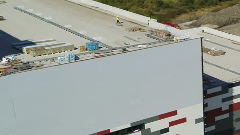 Aerial-view-of-construction-workers-looking-over-the-edge-of-a-high-roof-top-on-a-power-station-construction-site