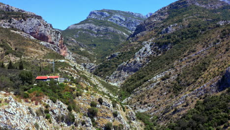 Rocky-mountain-ridge-near-Stari-Bar-town,Montenegro,with-trees-and-bushes-covering-the-steep-dry-mountainside,cliffs-and-hills-above-the-gorge,houses-with-red-rooftops-and-utility-poles-on-the-left