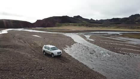 Four-Wheel-SUV-Vehicle-in-Wilderness-of-Icelandic-Highlands,-Aerial-View-of-Fourwheeler-Crossing-Over-Glacial-Stream