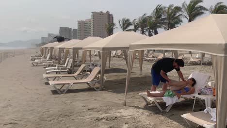 Massage-Am-Strand-Von-Acapulco,-Mexiko,-Weibliche-Touristin-Entspannt-Sich-Unter-Einem-Sonnenschirm,-Statische-Aufnahme