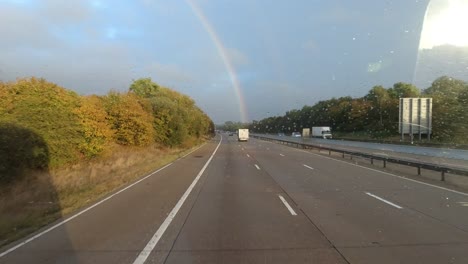 HGV-windscreen-view-of-traffic-driving-towards-a-rainbow-on-the-M20-motorway,-Kent