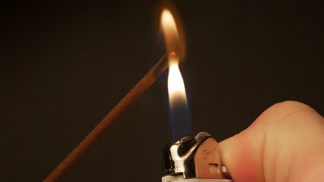 Lighting-The-End-Of-An-Incense-Stick-With-A-Lighter-And-Gently-Blowing-Out-The-Flame-Creating-Smoke-And-A-Red-Glow---Close-Up-Shot