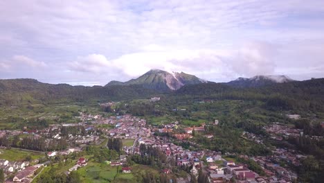 Hoch-Nach-Vorne-Fliegender-Drohnenschuss,-Der-über-Der-Stadt,-Dem-Dorf-Und-Dem-Grünen-Wald-Von-Berastagi-Mit-Blick-Auf-Den-Aktiven-Vulkan-Berg-Sibayak-Im-Norden-Sumateras-In-Indonesien-Reist