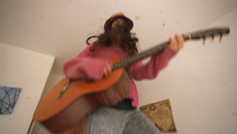 Young-Girl-Jumping-On-Bed-With-Guitar-In-Bedroom-at-Home