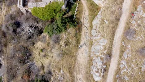 drone-shot-of-a-mountain-biker-riding-on-a-gravel-road-away-from-a-ruin-castle