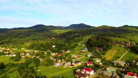 Aerial-view-over-houses,-forest-and-sunlit-green-nature,-in-Myhove-village,-of-the-Carpathian-Mountains,-golden-hour,-in-Ukraine---pan,-drone-shot