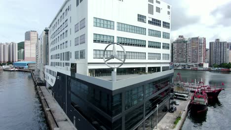 Large-Mercedes-Benz-sign-spinning-on-top-of-Hong-Kong-Mercedes-Benz-main-showroom-in-Chai-Wan-area,-Aerial-view