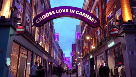 People-in-face-masks-walking-past-closed-stores-underneath-Covid-pandemic-themed-Christmas-lights-on-Carnaby-Street-in-London’s-West-End