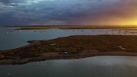 An-aerial-flight-over-the-salt-marshes-at-West-Mersea,-Essex-just-before-a-storm-with-dramatic-light-over-the-water
