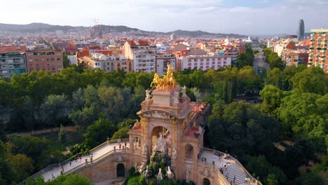 Aerial-view-of-the-Cascada-Monumental-golden-statue-and-fountain,-in-the-Ciutadella-park,-Barcelona,-Spain,-during-sunset---reverse-,drone-shot