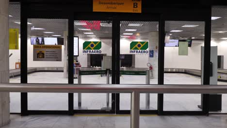 Tilt-down-from-arrival-and-departure-board-to-closed-doors-and-empty-arrival-hall-with-baggage-claim-conveyer-belt-in-the-background