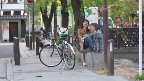 Two-Japanese-Friend-Sitting-On-The-Concrete-Bench,-Chatting-And-Having-A-Good-Time-While-Smoking-On-The-Street-In-Kyoto,-Japan
