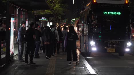 Menschen-Mit-Maske-An-Der-Bushaltestelle-Im-Bezirk-Gangnam,-Seoul-Bei-Nacht-–-Mittlere-Einstellung