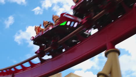 Rollercoaster-with-screaming-people-riding-up-and-down-on-red-rail-track