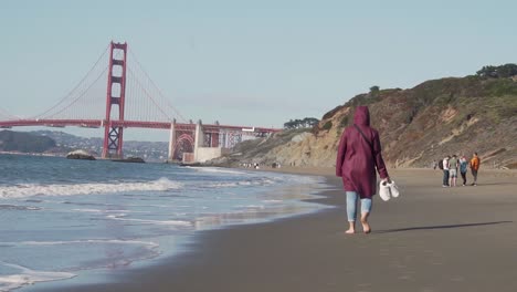 Tourist-Walking-on-Sandy-Beach-by-Pacific-Ocean-With-View-of-Golden-Gate-Bridge-San-Francisco,-California-USA